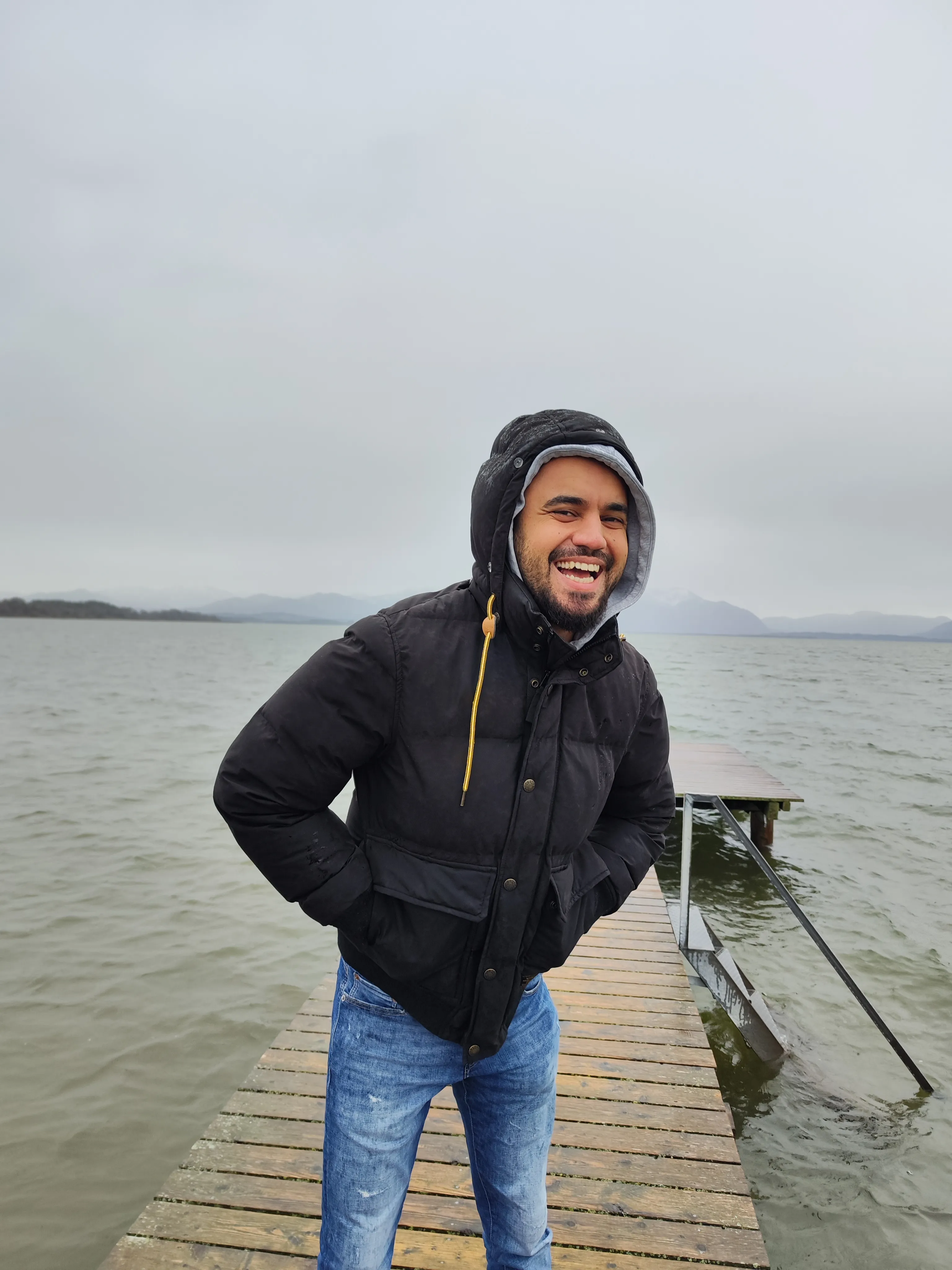 Ashkan Vahdani lachend auf einem Holzsteg am Chiemsee